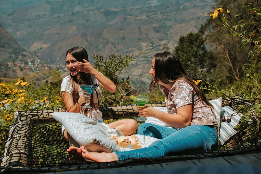 Two friends enjoy drinks on a hammock with stunning Cáqueza views. Perfect travel and leisure moment.