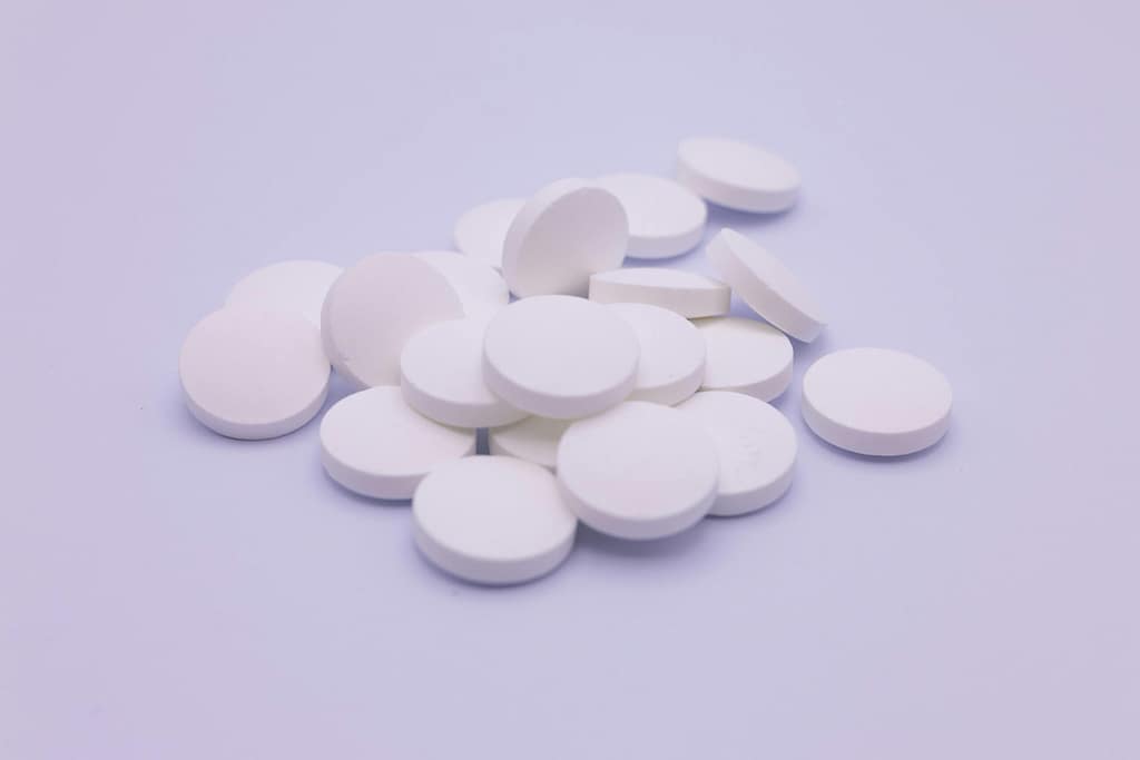 Assorted white tablets stacked on a soft purple surface, symbolizing medication and healthcare.