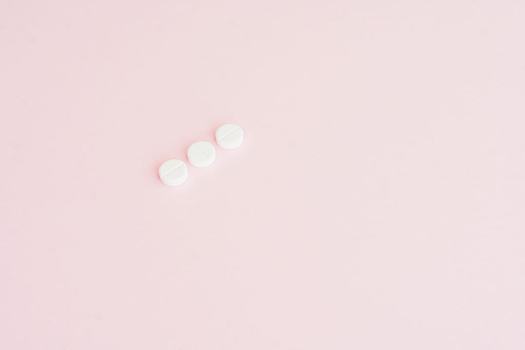 Simple minimalist image showing three white pills on a pastel pink background, ideal for health themes.