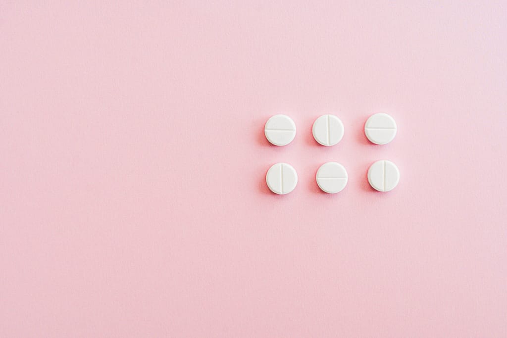 Minimalistic arrangement of white pills on a soft pink background.