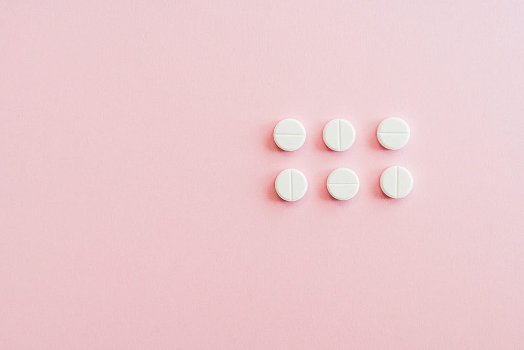 Minimalistic arrangement of white pills on a soft pink background.
