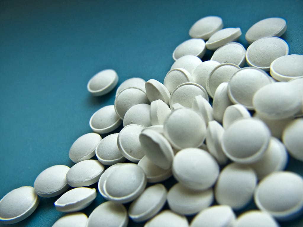 High angle of white round tablets for disease treatment scattered on blue background