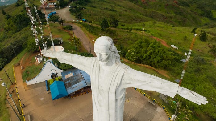A stunning aerial photo of the Cristo Rey statue on a lush hillside in Colombia.