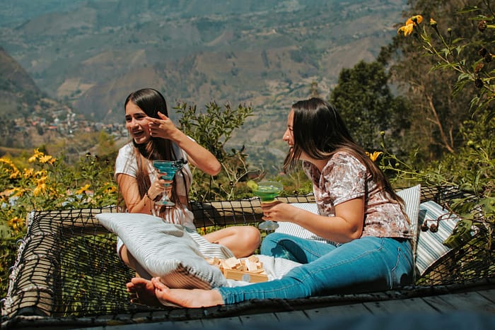 Two friends enjoy drinks on a hammock with stunning Cáqueza views. Perfect travel and leisure moment.