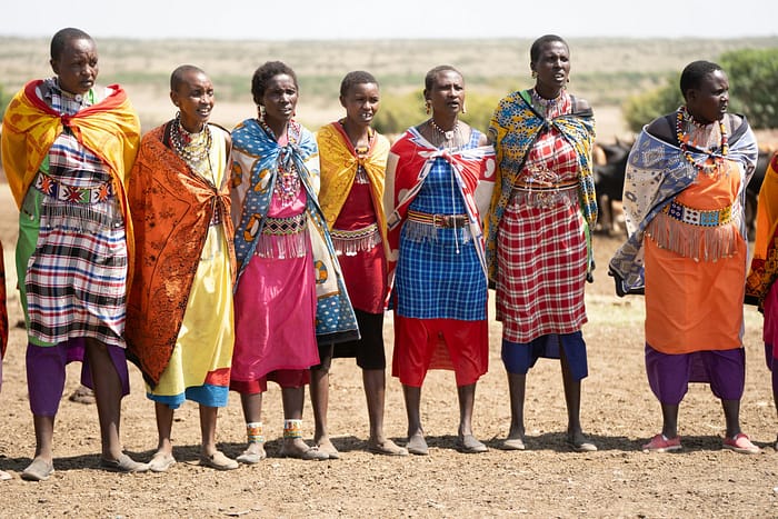 Maasai women in traditional attire showcasing colorful cultural fashion in a Kenyan landscape.