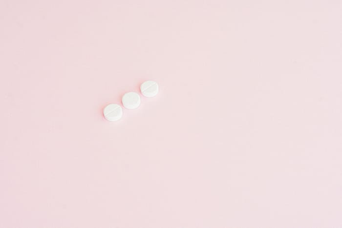 Simple minimalist image showing three white pills on a pastel pink background, ideal for health themes.